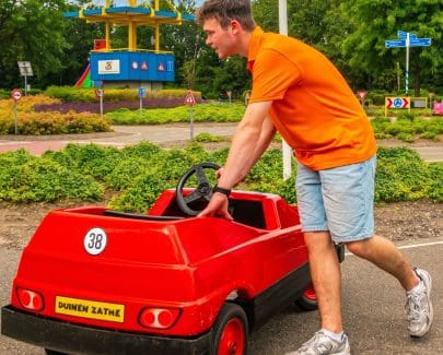 Een medewerker van Duinen Zathe duwt een rode auto op het Verkeerscircuit.